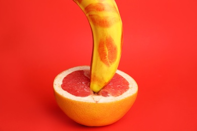 Photo of Fresh grapefruit and banana with lipstick marks on red background. Sex concept
