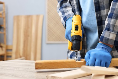 Young handyman working with electric drill at table in workshop, closeup