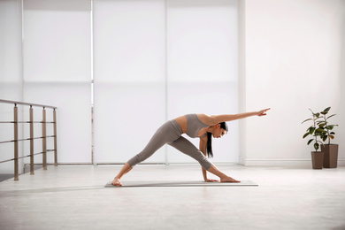 Photo of Young woman practicing triangle asana in yoga studio. Utthita Trikonasana pose