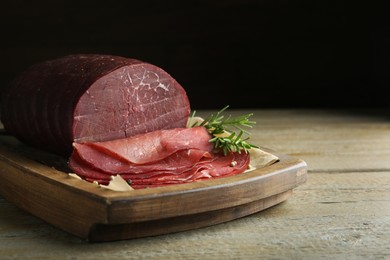 Photo of Tasty bresaola, peppercorns and rosemary on wooden table, closeup. Space for text