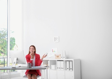 Photo of Happy young woman operating air conditioner with remote control in office