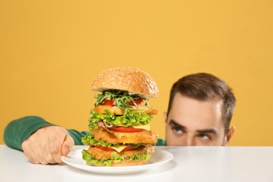 Photo of Young hungry man and huge burger on color background