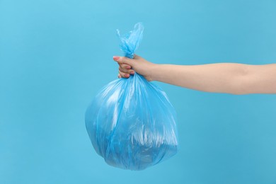 Photo of Woman holding plastic bag full of garbage on light blue background, closeup