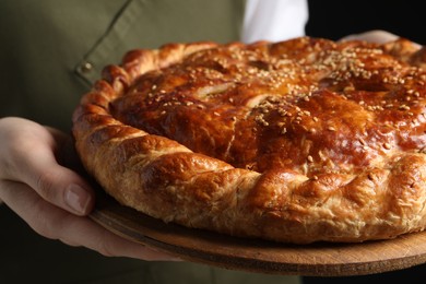 Photo of Woman holding tasty homemade pie on black background, closeup