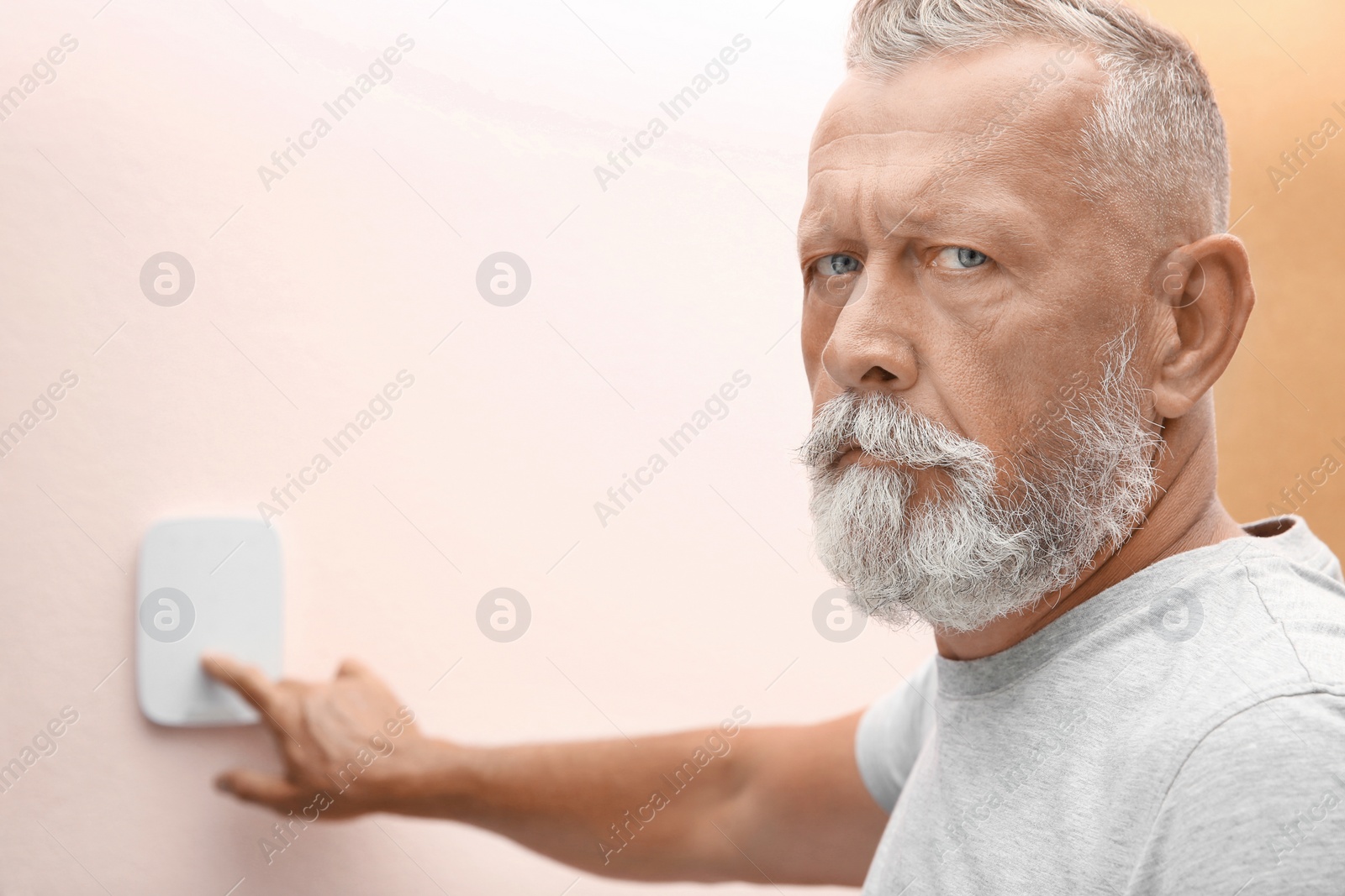 Photo of Mature man entering code on alarm system keypad indoors