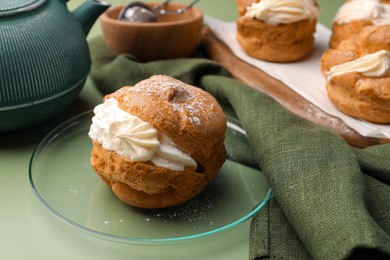 Delicious profiteroles filled with cream on green background, space for text