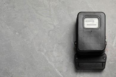 Photo of Black electric meter on light grey marble background, top view with space for text. Measuring device
