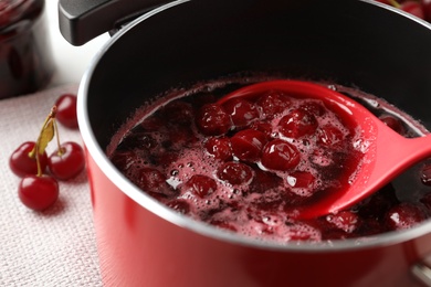 Photo of Pot with cherries in sugar syrup on table, closeup. Making delicious jam
