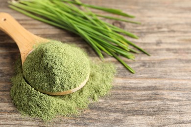 Photo of Wheat grass powder in spoon on wooden table, closeup. Space for text