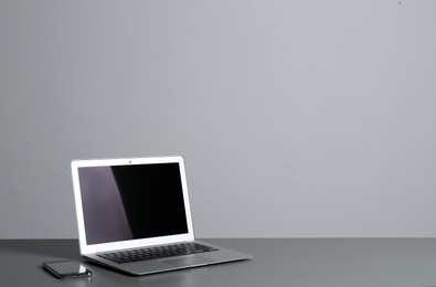 Photo of Modern laptop with blank screen and mobile phone on table against gray background