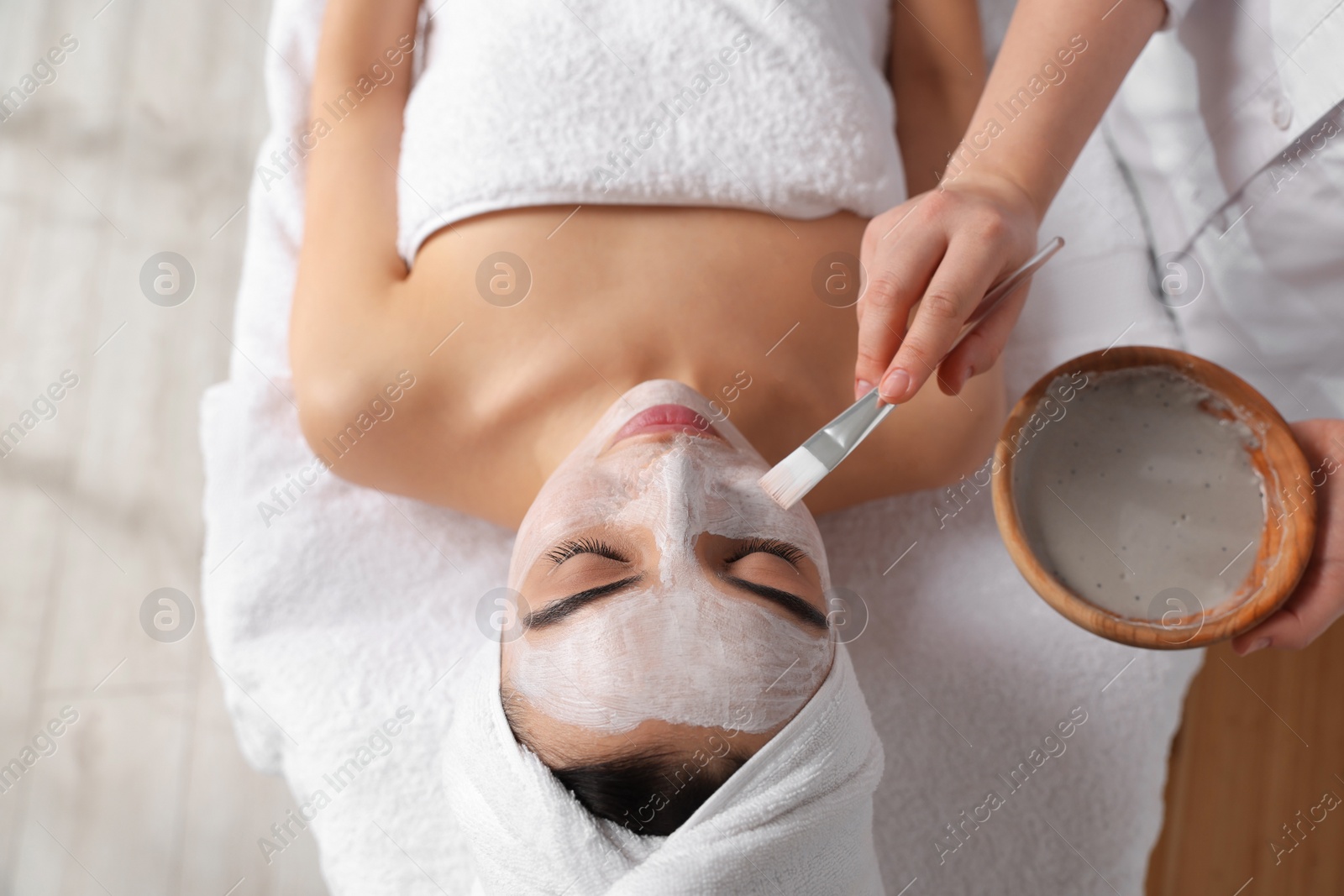 Photo of Cosmetologist applying mask on woman's face in spa salon, above view