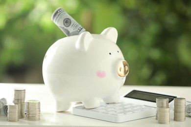 Financial savings. Piggy bank with dollar banknotes, stacked coins and calculator on white wooden table outdoors