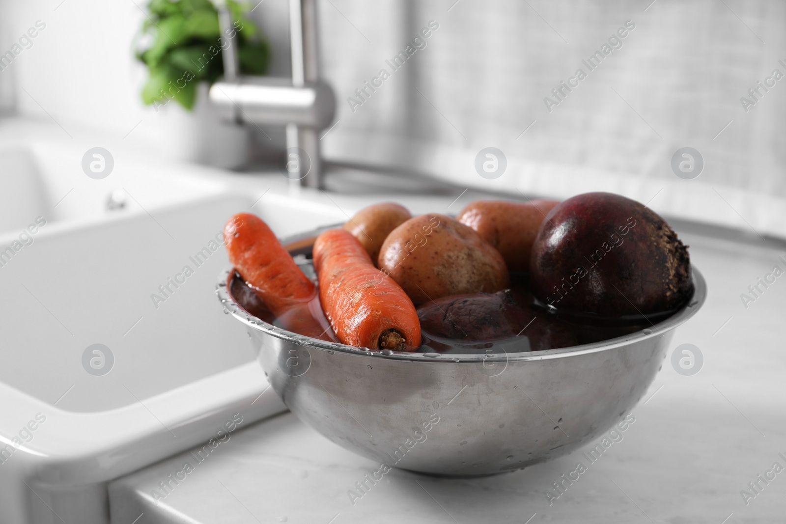 Photo of Fresh vegetables with water in bowl on white countertop. Cooking vinaigrette salad