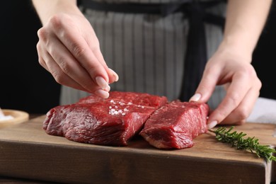Photo of Woman salting fresh raw beef steak at table, closeup