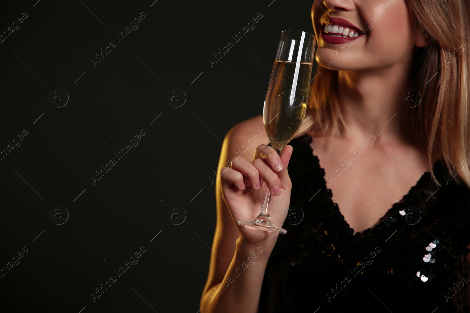 Photo of Beautiful woman with glass of champagne on dark background, closeup. Space for text