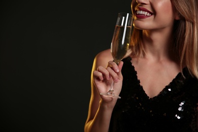 Beautiful woman with glass of champagne on dark background, closeup. Space for text