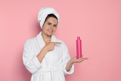 Photo of Beautiful young woman holding bottle of shampoo on pink background