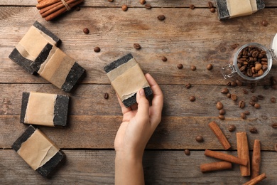 Woman holding handmade soap bar over table with ingredients, top view