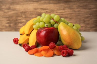 Photo of Delicious ripe fruits, raspberries and dried apricots on beige table