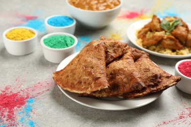 Photo of Traditional Indian food and color powders on grey table. Holi festival celebration