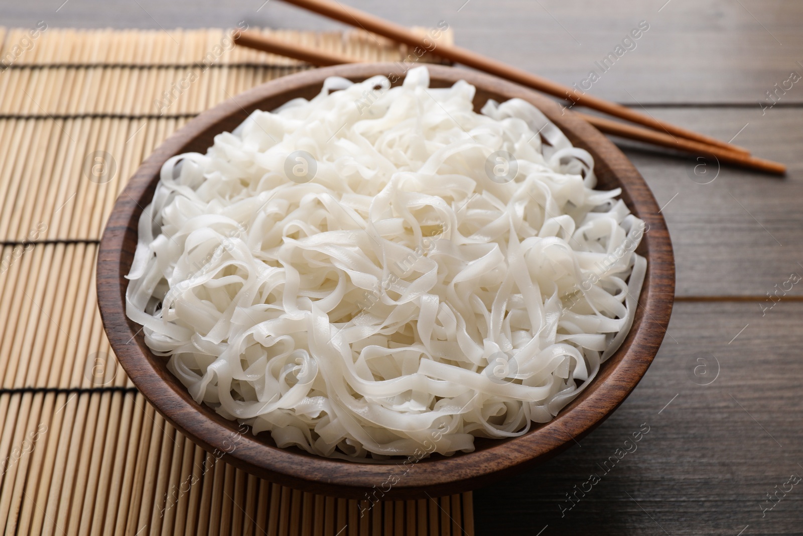 Photo of Bowl of tasty cooked rice noodles and chopsticks on wooden table