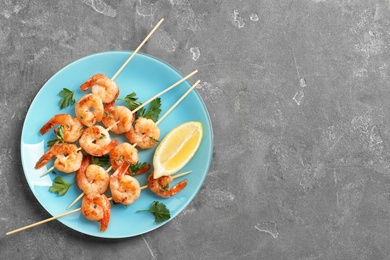 Photo of Plate with delicious fried shrimp skewers and lemon on grey background, top view