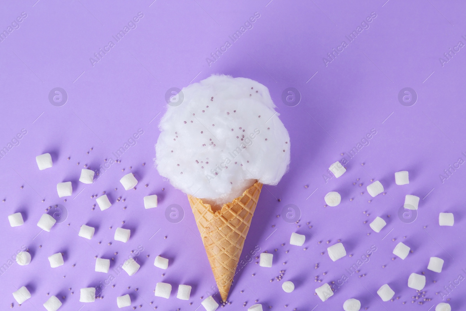 Photo of Sweet cotton candy in waffle cone and marshmallows on purple background, flat lay