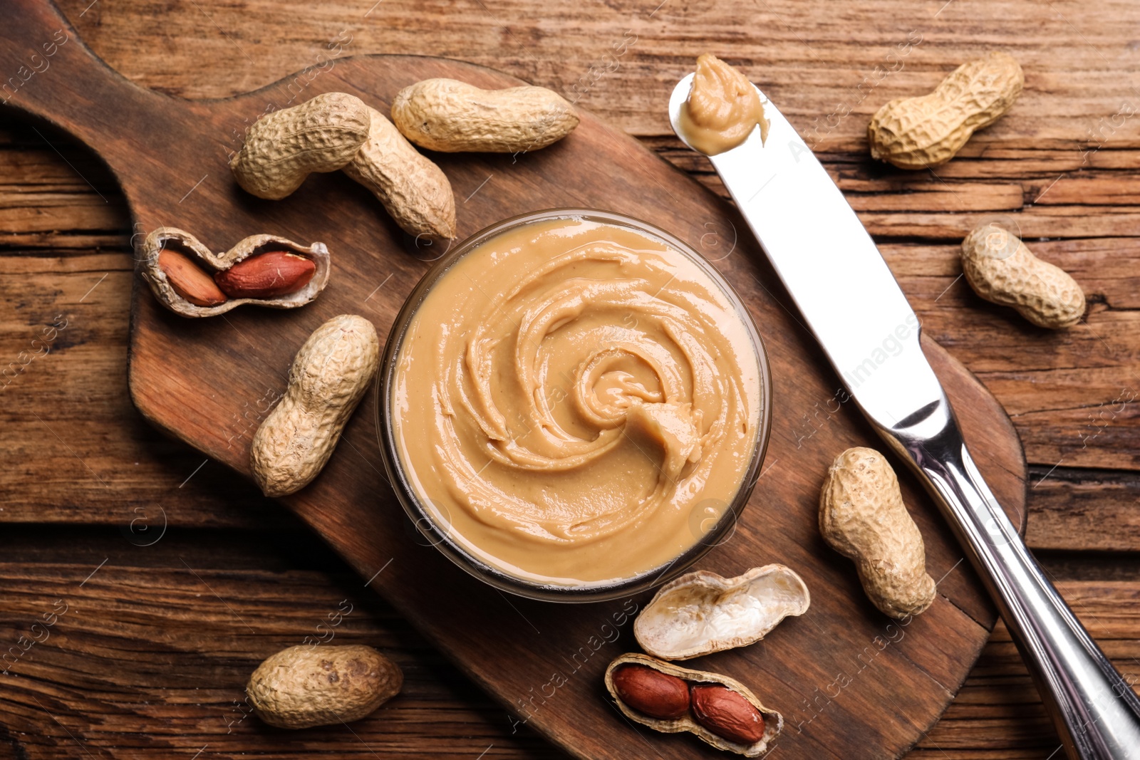 Photo of Yummy peanut butter in glass bowl on wooden table, flat lay