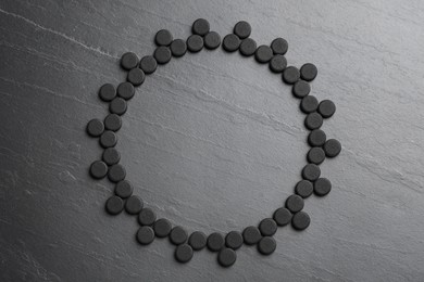 Frame of activated charcoal pills on black table, flat lay with space for text. Potent sorbent