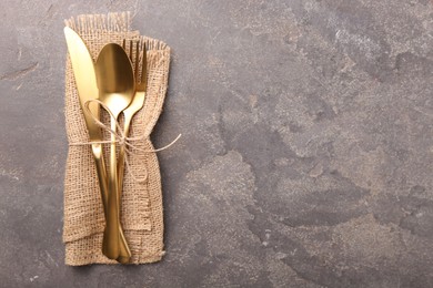 Set of stylish cutlery and napkin on grey textured table, top view. Space for text