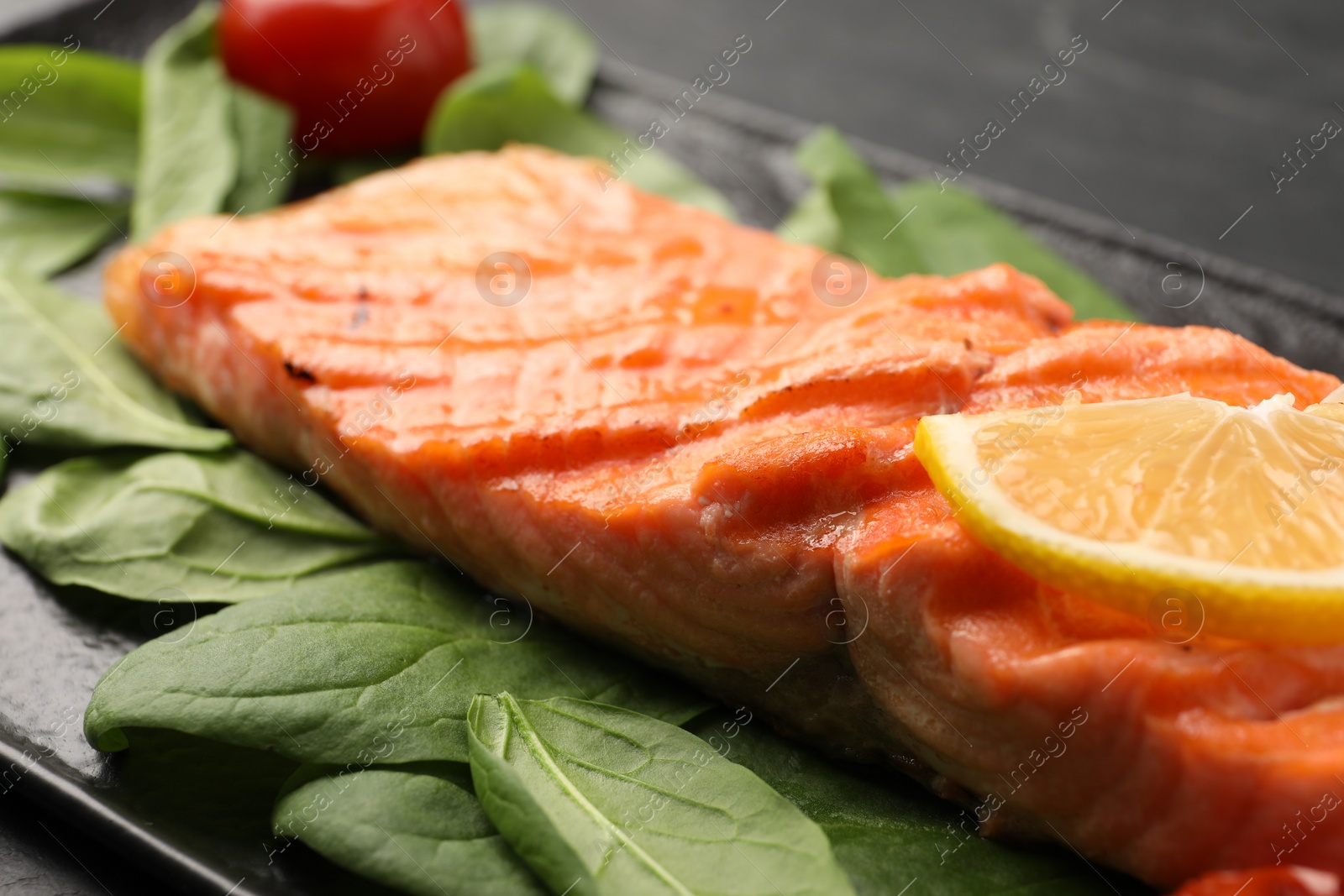 Photo of Tasty grilled salmon with lemon and spinach on table, closeup