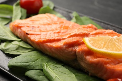 Tasty grilled salmon with lemon and spinach on table, closeup