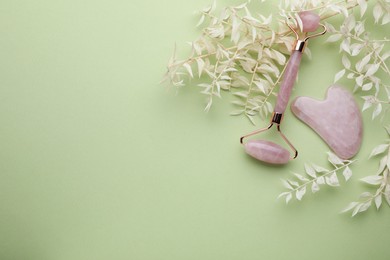 Photo of Rose quartz gua sha tool and facial roller on light green background, flat lay. Space for text