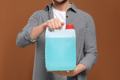 Photo of Man holding canister with blue liquid on brown background, closeup