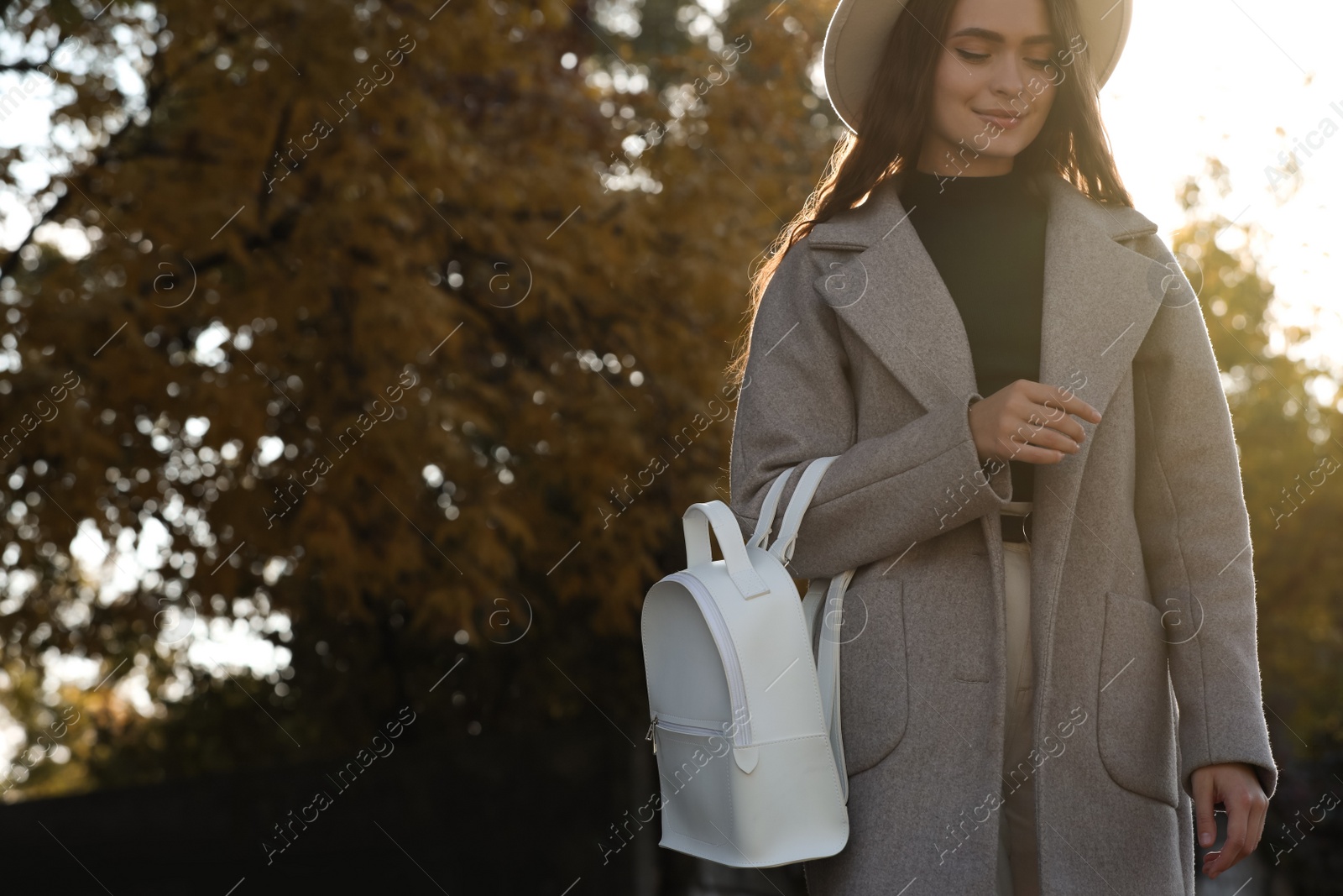 Photo of Young woman with stylish white backpack in park, space for text