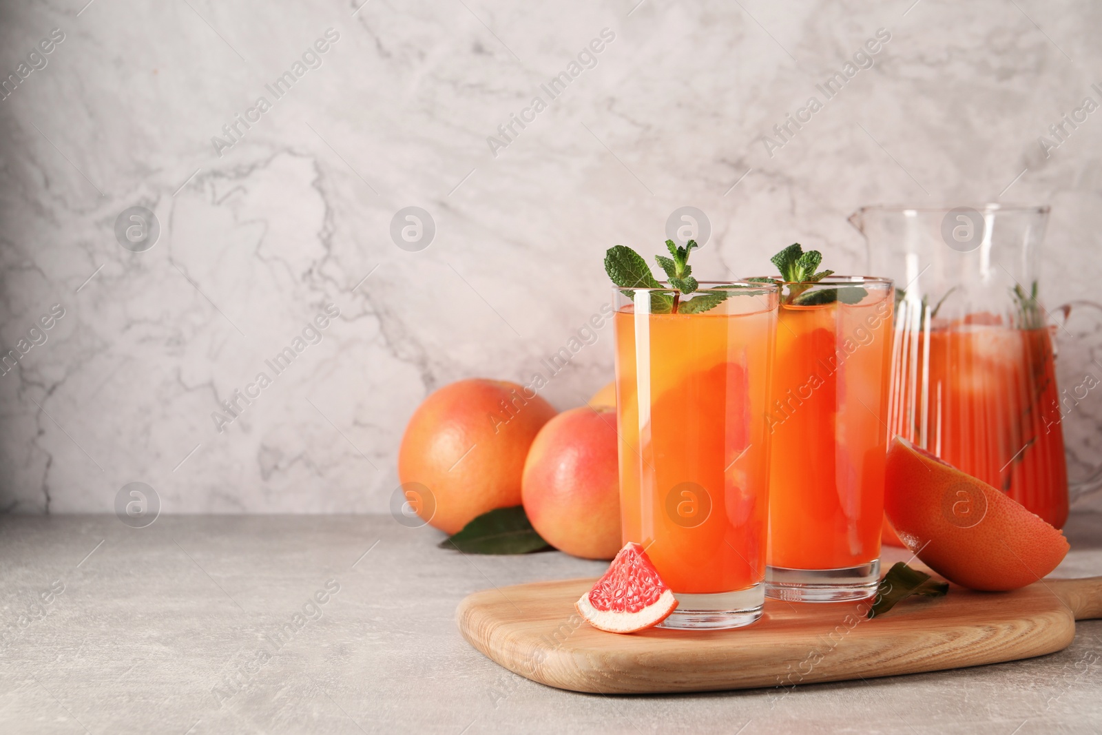 Photo of Tasty freshly made grapefruit juice, fruits and mint on light grey table, space for text