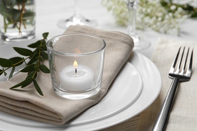 Stylish setting with cutlery, burning candle and eucalyptus leaves on white wooden table, closeup