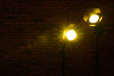 Photo of Bright yellow spotlights near brick wall in darkness, space for text