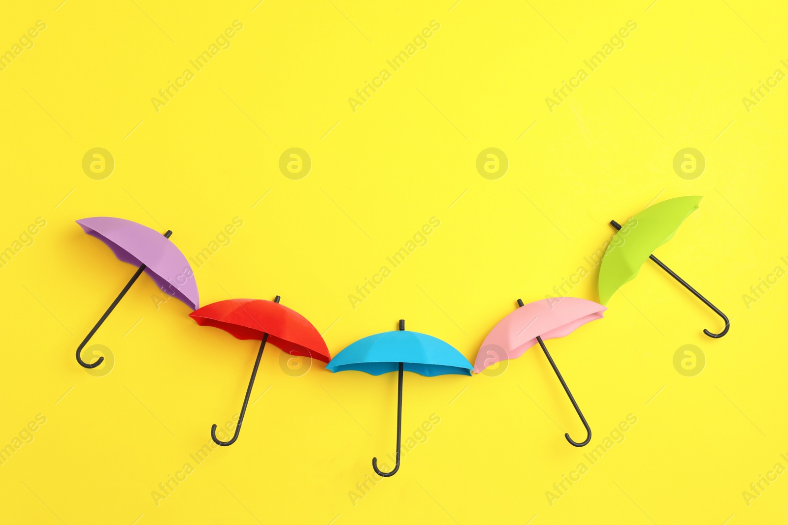 Photo of Bright toy umbrellas on yellow background, flat lay