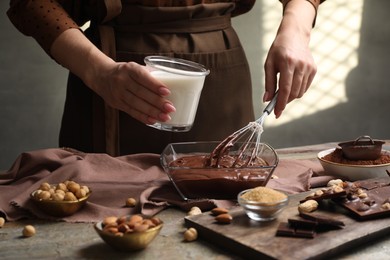 Photo of Woman with glass of milk and whisk mixing delicious chocolate cream at textured table, closeup