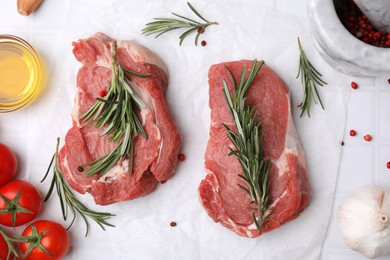 Fresh raw meat with rosemary, oil, tomatoes and spices on white tiled table, flat lay
