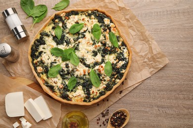 Delicious homemade spinach quiche and ingredients on wooden table, flat lay