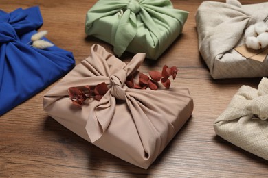 Photo of Furoshiki technique. Many gifts packed in fabric and dry leaves on wooden table