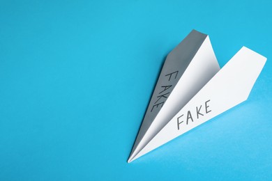 Photo of Paper plane with words FAKE on light blue background, top view. Space for text
