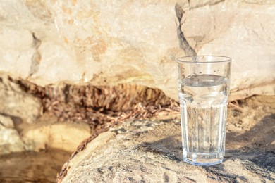 Glass of clean water on rock outdoors. Space for text