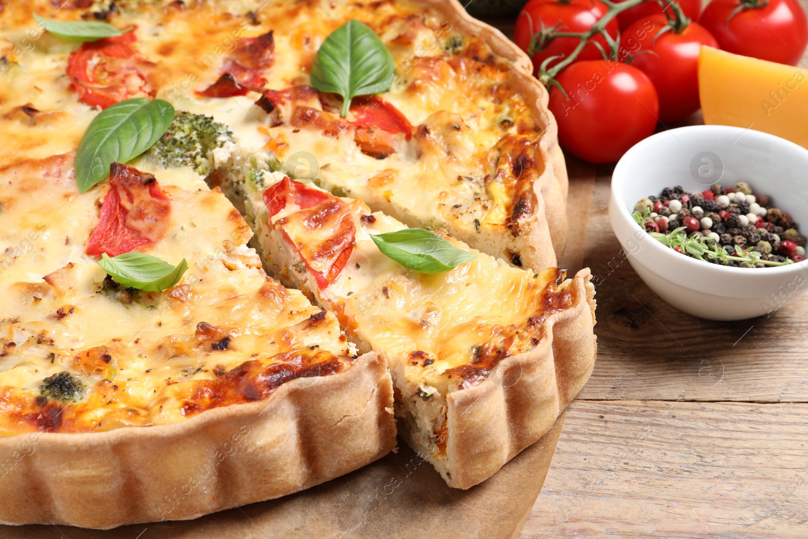 Photo of Tasty quiche with tomatoes, basil and cheese served on wooden table, closeup