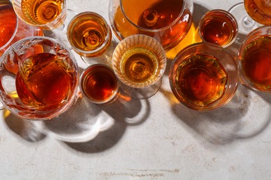 Photo of Different delicious liqueurs in glasses on light grey table, flat lay