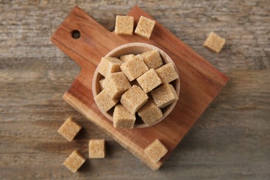 Photo of Bowl with brown sugar cubes on wooden table, flat lay