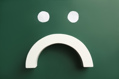Photo of Sad face on green chalkboard, flat lay