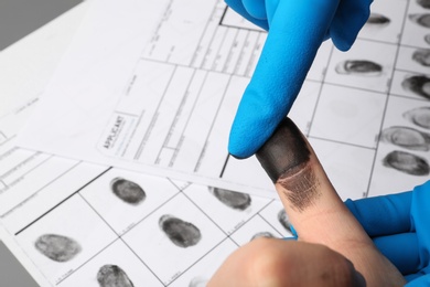 Investigator taking fingerprints of suspect at table, closeup with space for text. Criminal expertise